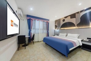 Une chambre d’hôtel avec un lit, un bureau et une chaise. Il y a un téléviseur fixé au mur et une fenêtre avec des rideaux.