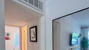 A hallway with a bed, a framed picture, a television, and a pineapple decoration. - Cozy 2 BR Condo - 7 Min from Fort Lauderdale Beach (Fort Lauderdale)