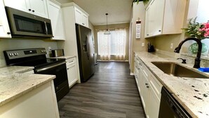 Una cocina con gabinetes blancos, microondas, estufa, refrigerador y lavavajillas.