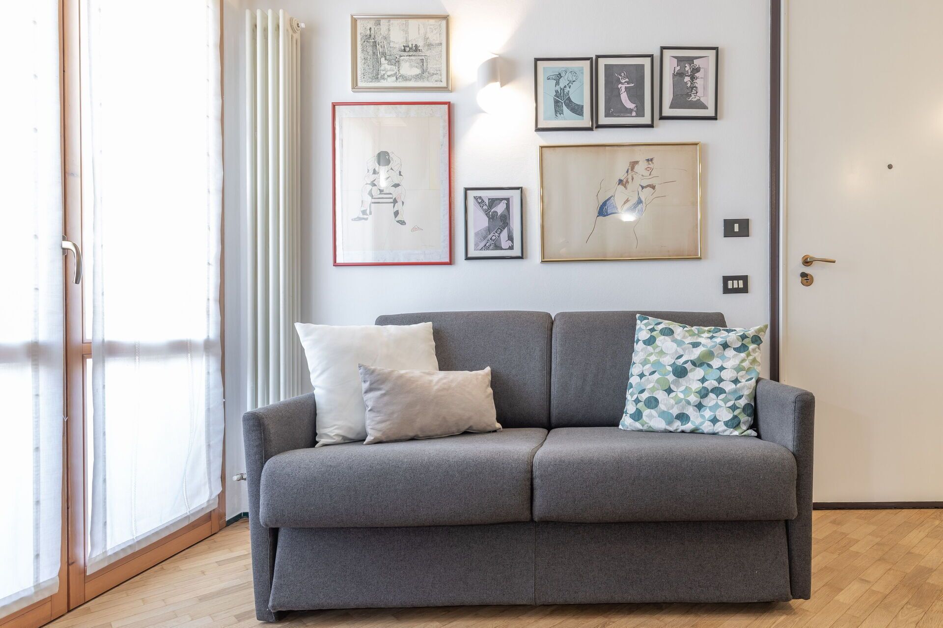 A grey sofa with two pillows, a radiator, and several framed artworks on the wall.