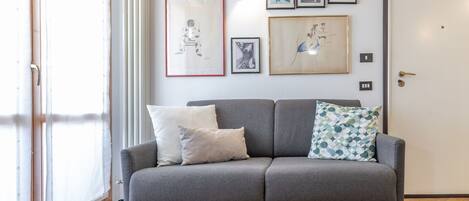 A grey sofa with two pillows, a radiator, and several framed artworks on the wall.