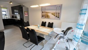 Une cuisine moderne avec des meubles de couleur sombre, une table à manger avec des chaises et un transat pour bébé.