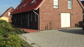 Une maison en briques avec un toit recouvert de tuiles rouges, un garage et une allée pavée.
