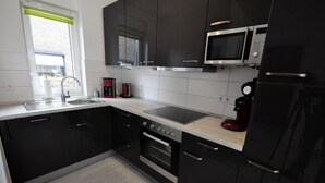 Une cuisine moderne avec des meubles noirs, un évier en acier inoxydable, un four à micro-ondes, une machine à café rouge et un four.
