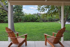 A covered patio with two wooden Adirondack chairs facing a well-maintained lawn. - Denver 3bed/2 bath with spacious backyard (Arvada)