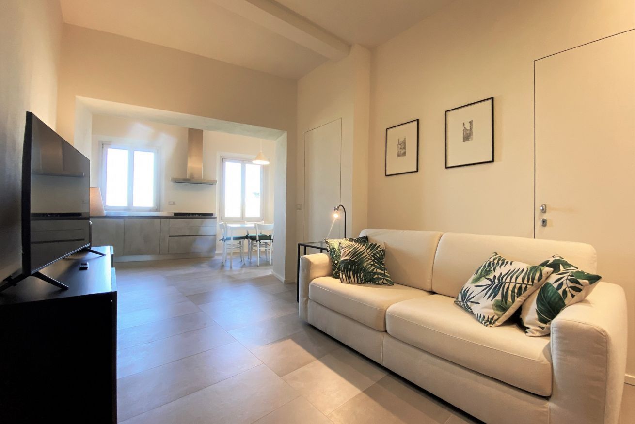 A modern living room with a sofa, a flat-screen TV, and a dining area in the background.