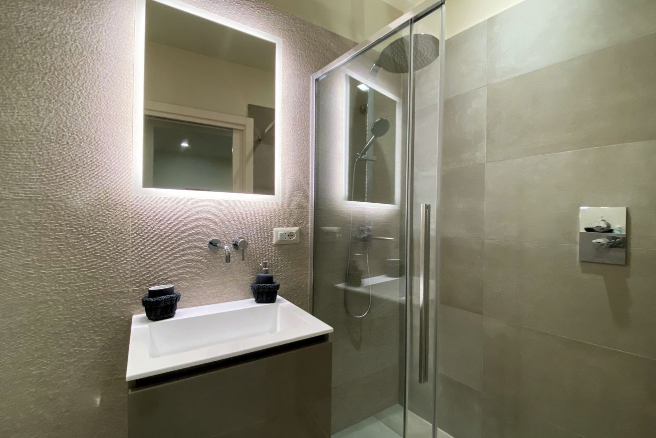Un baño moderno con ducha envuelta en cristal, un lavabo blanco y un espejo grande.