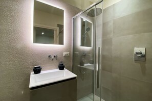 Une salle de bain moderne avec une douche à parois de verre, un lavabo blanc et un grand miroir.