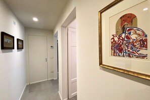 A hallway with white walls, a framed abstract painting, and a door at the end. - TRA LE MURA – Downtown Apartment in Siena (Siena)