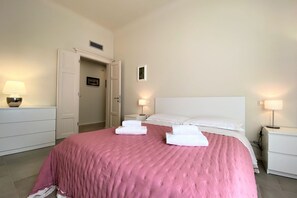 A hotel room with a bed, white nightstands, a door, and a small picture on the wall. - TRA LE MURA – Downtown Apartment in Siena (Siena)