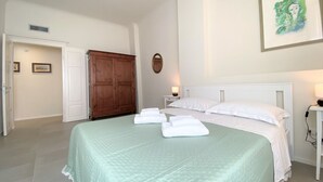 Ein ordentlich bezogenes Bett mit weißen Leinen, ein Holzschrank und ein gerahmtes Bild an der Wand.