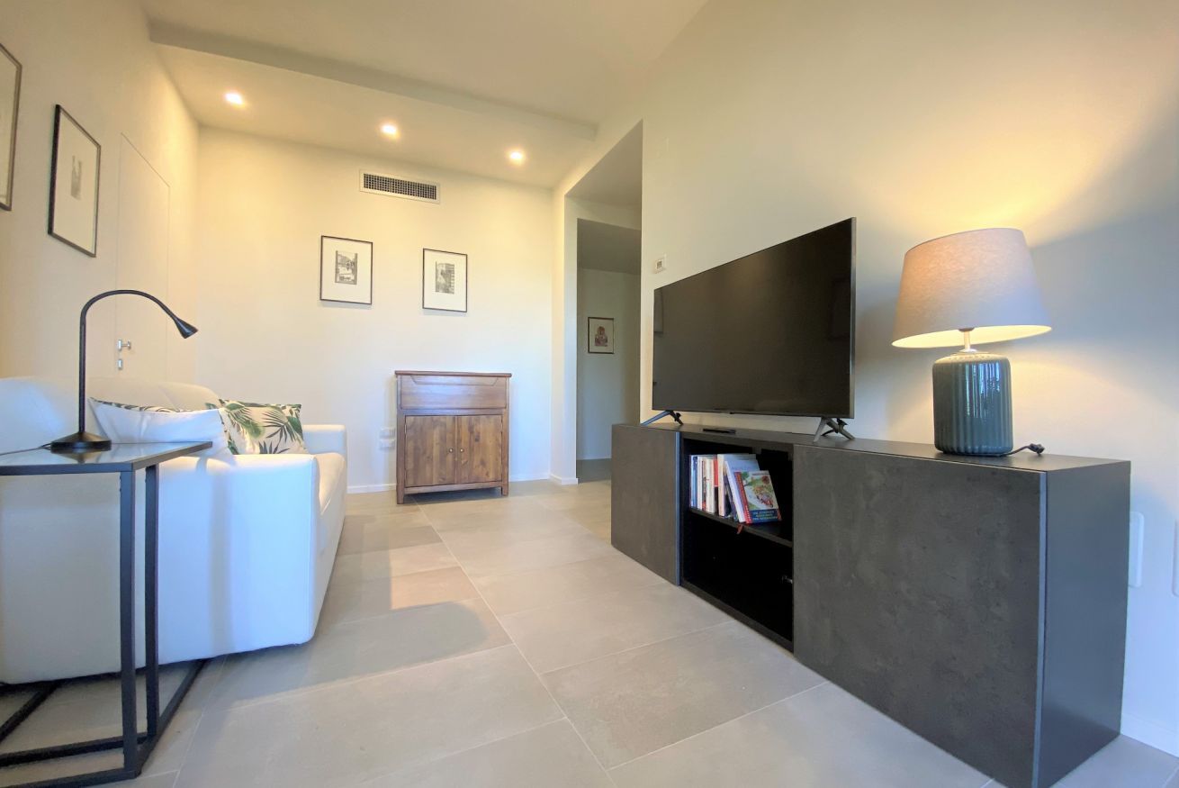 Una sala de estar moderna con un sofá, una mesa de centro, un televisor sobre un mueble, una lámpara y una estantería.