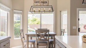 A kitchen with a dining table and chairs, a hanging light fixture, and a window with a view of greenery. - Cave Creek Gem: Heated Pool, Sleeps 8 (Cave Creek)