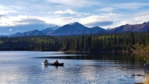 Un lac paisible où flottent deux canoës, entouré d’une forêt dense et dominé par des montagnes en arrière-plan.