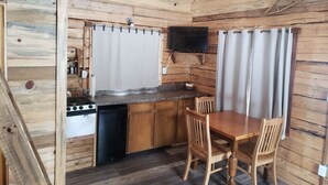 Une cuisine compacte aux murs en bois, dotée d’une cuisinière intégrée, d’un lave-vaisselle et d’un téléviseur à écran plat fixé au-dessus d’un comptoir.