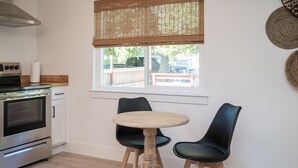 Eine Küche mit Backofen, einem Esstisch mit zwei Stühlen und einem Fenster mit Bambusrollvorhang.