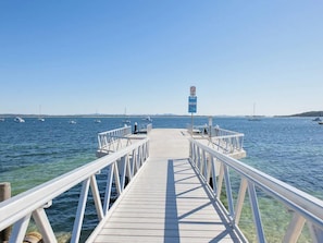 Un muelle de madera que se adentra en aguas tranquilas, con barcos al fondo.