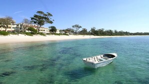 Ein Boot vor Anker in der Nähe eines Strandes mit klarem Wasser, sandigem Ufer und Gebäuden im Hintergrund.