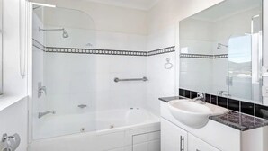 Ein modernes Badezimmer mit einer gläsernen Duschkabine, einer weißen Badewanne und einem Waschtisch mit großem Spiegel.