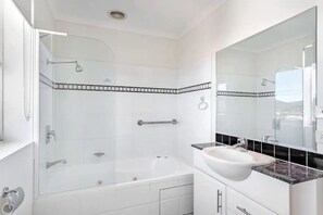 Un baño moderno con ducha de vidrio, una bañera blanca y un tocador con un espejo grande.