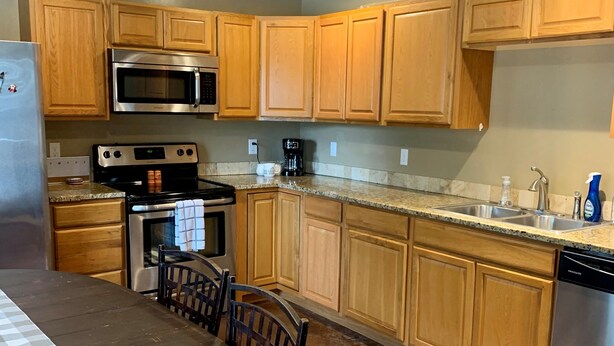 A kitchen with wooden cabinets, a stainless steel refrigerator, a microwave, an oven, a coffee maker, and a dishwasher.