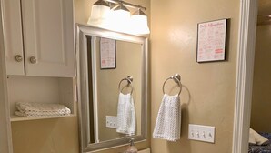 A bathroom with a toilet, sink, and mirror. There are towels hanging on the wall and a framed picture.