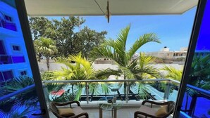 Ein Balkon mit zwei Korbstühlen und einem kleinen Tisch, mit Blick auf eine Wohngegend mit Palmen und Häusern.