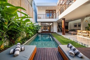 Ein modernes Haus mit Swimmingpool, Holzterrasse und Sitzbereich im Freien.