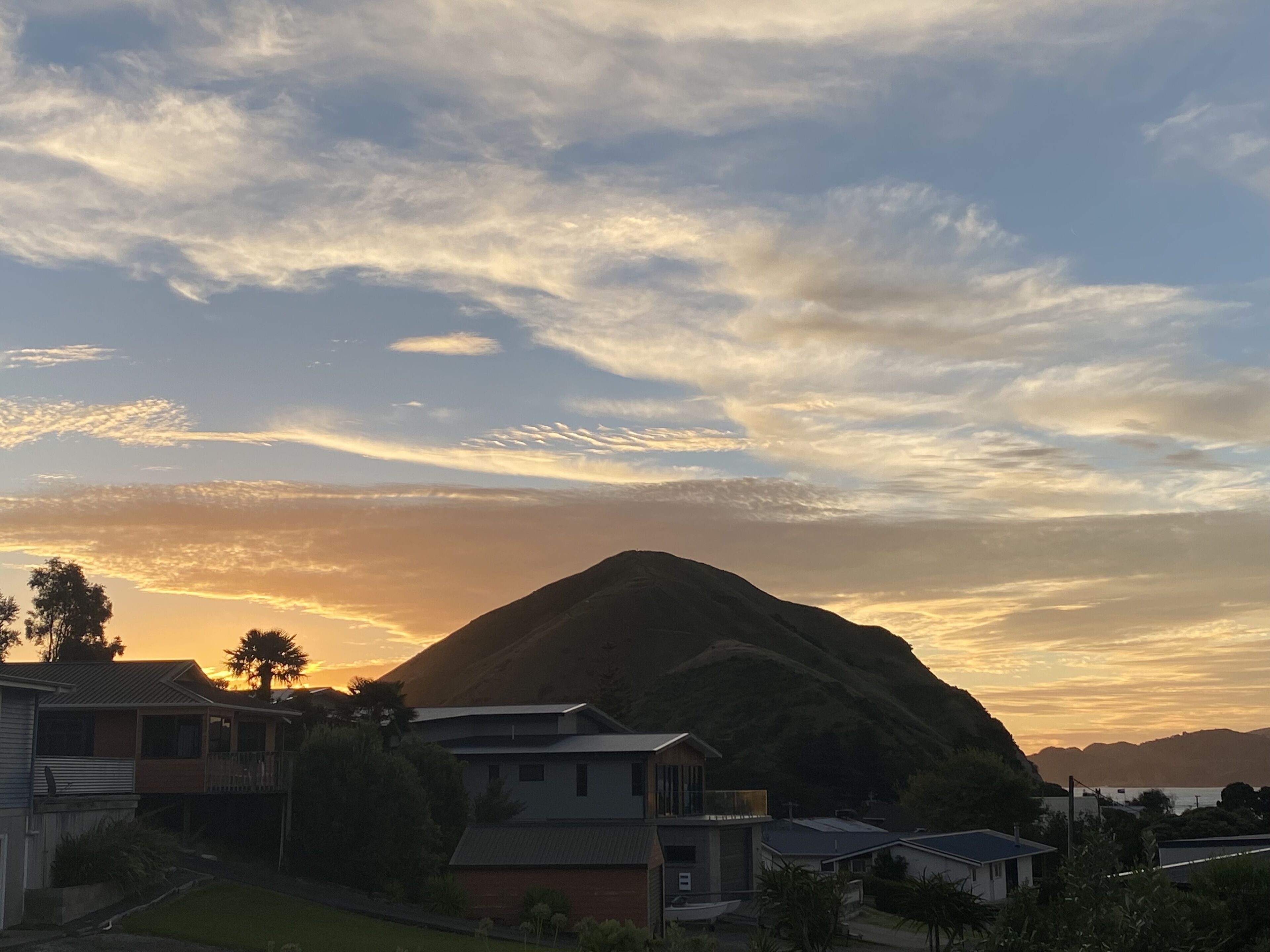 A residential area with houses, a prominent hill, and a sunset sky.