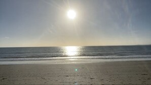 A beach with a clear sky and the sun shining over the water.