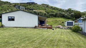 A residential area with a white house, a covered porch, and a hill with vegetation.