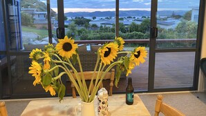 A table with a vase of sunflowers, a decorative mug, and a bottle of beer on a balcony with a view of a mountainous landscape.