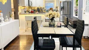 A modern kitchen with white cabinets, a dining area with black chairs, and a large window.