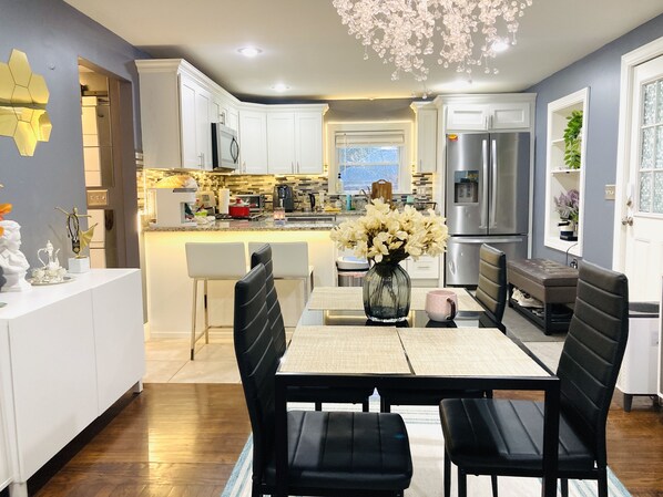 A modern kitchen with white cabinets, a dining area with black chairs, and a large window.