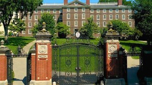 A large brick building with a central entrance gate, surrounded by well-maintained lawns and trees.