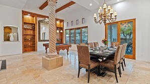 Uma área de jantar ampla com mesa de bilhar, lustre e uma grande janela com vista para o exterior.