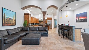 Ampla sala de estar com sofá de couro em formato de canto, cozinha com armários de madeira e área de bar com banquetas.