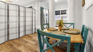 Un coin repas avec une table en bois, des chaises de couleur turquoise, des sets de table en fibres tressées et un vase rempli de fleurs.