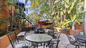 Une terrasse extérieure avec des meubles en métal, une table ronde et un espace barbecue entouré d’une végétation luxuriante.