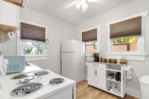 A compact kitchen with a white stove, a refrigerator, and a small countertop with kitchenware. - The Palms of Tampa - Private Courtyard (Tampa)