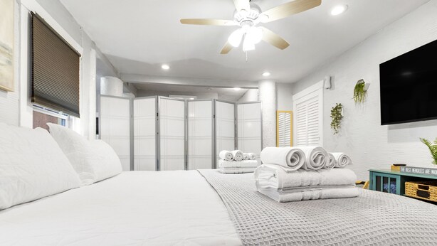 Une chambre moderne dotée d’un grand lit, d’un ventilateur de plafond, d’un téléviseur à écran plat et d’une armoire aux portes coulissantes.