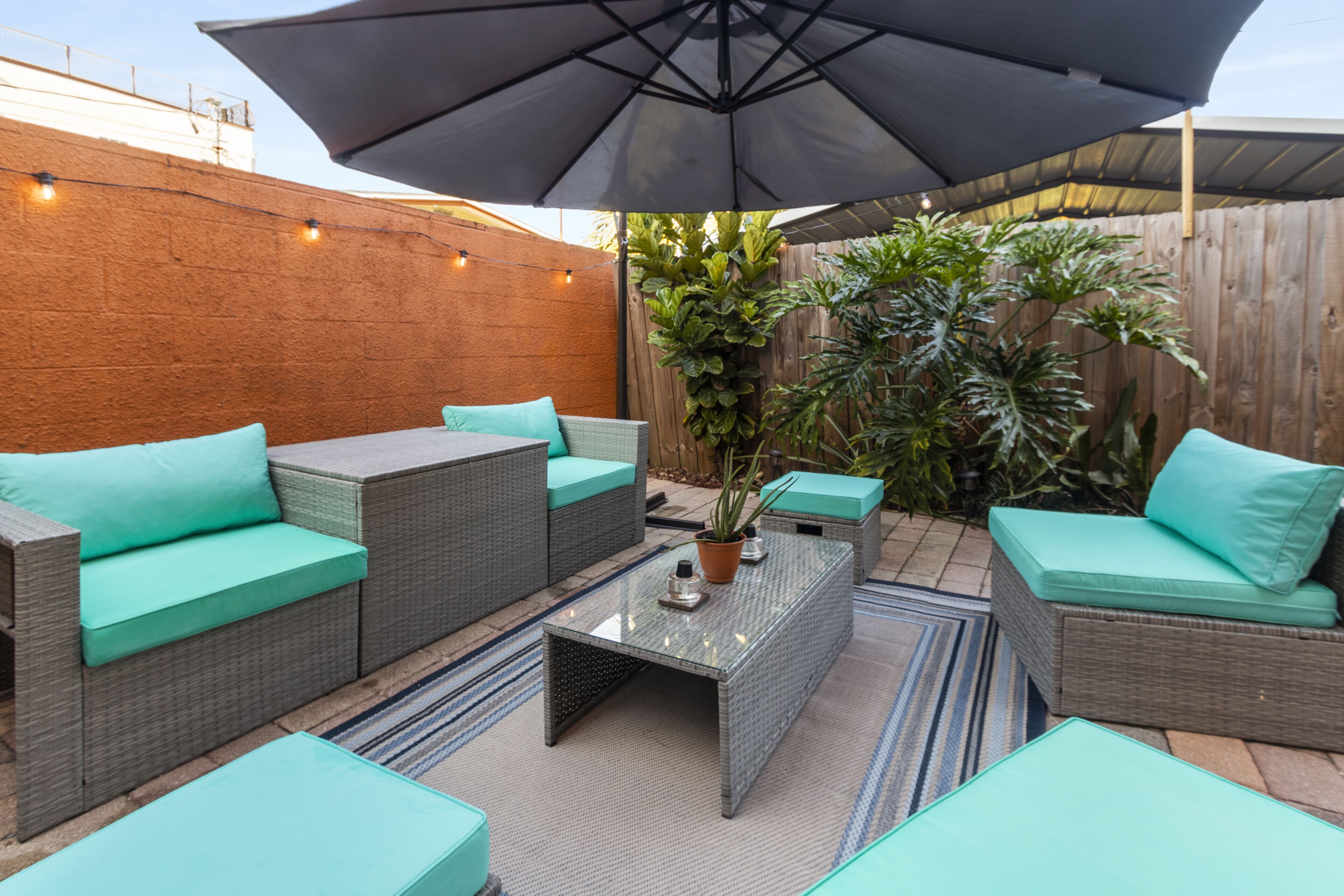 An outdoor patio area with wicker furniture, a glass-top coffee table, and a large umbrella.