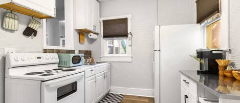 A kitchen with white cabinets, a stove, a microwave, and a refrigerator.