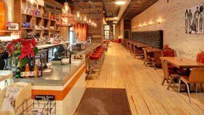 A restaurant with a bar area, wooden tables, and a brick wall.
