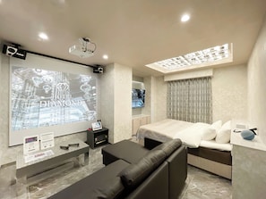 Quarto de hotel moderno com uma grande tela exibindo 'HOTEL DIAMOND', uma cama, um sofá, uma TV e uma luminária de teto.