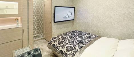 A bedroom with a bed, a TV mounted on the wall, a wardrobe, and a bathroom with a shower.