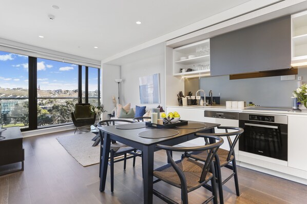 A modern kitchen with a dining area, large windows, and a city view.