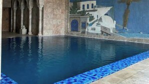 Una piscina con borde de azulejos, un mural con detalles arquitectónicos y una pared de piedra.
