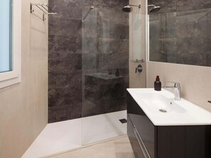 Un baño moderno con ducha envuelta en vidrio, un lavamanos blanco y un espejo grande.