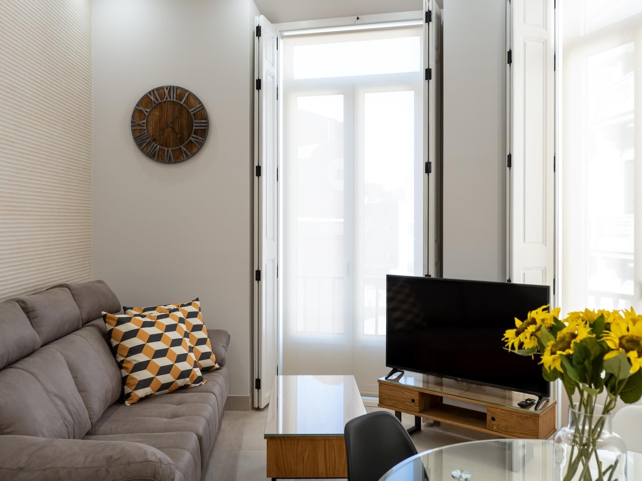 Un salon moderne avec un canapé, un téléviseur à écran plat, une table basse en verre et une horloge murale décorative.